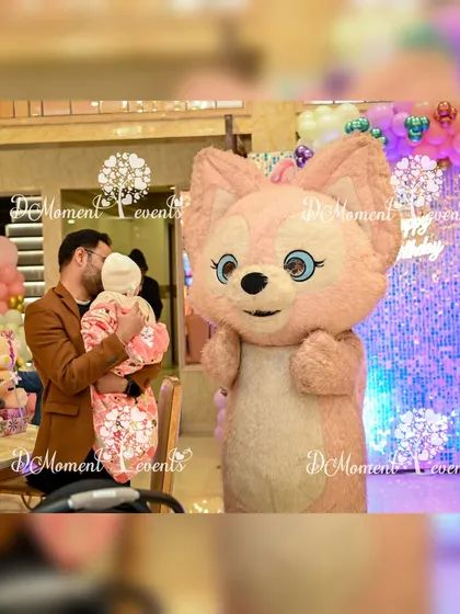 A candid moment as a cute pink fox mascot interacts with the birthday baby and her father, creating a sweet memory.