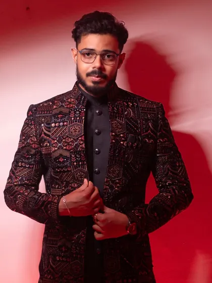 A groom's portrait that is all about style and confidence. The bold red background highlights the intricate details of his sherwani, creating a powerful, modern look.