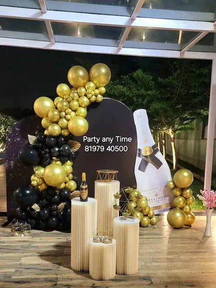 A fun and glamorous champagne-themed decoration. The setup includes a giant champagne bottle cutout and a black and gold balloon garland.