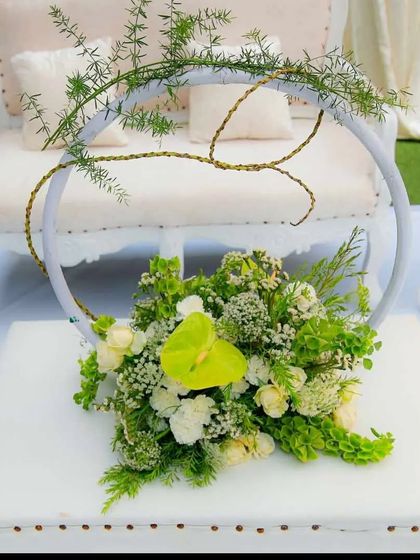 A unique and modern floral centerpiece. This arrangement uses a mix of green and white flowers with delicate foliage, designed within a circular frame for a contemporary touch on the guest seating.