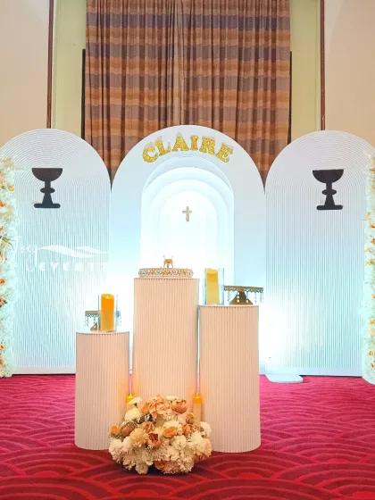 A clean and modern stage we created for a First Holy Communion. This setup uses textured white arched panels, minimalist chalice symbols, and warm floral arrangements to create a sophisticated and reverent atmosphere.
