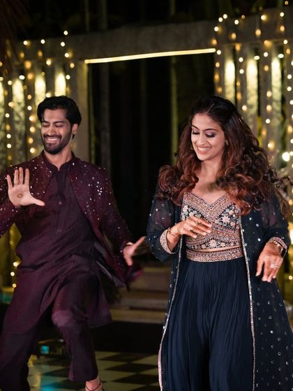 A candid photo of the groom and his sister dancing, their smiles illuminated by the warm, festive lights of the Sangeet decor.