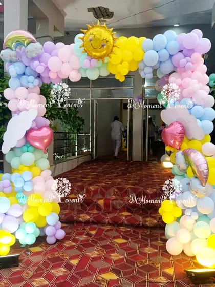A bright and happy entrance arch for a rainbow and sunshine themed party. The pastel balloon arch is accented with a smiling sun, a rainbow, and fluffy cloud details.