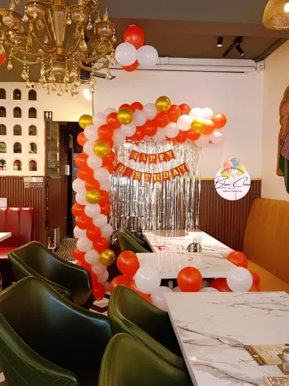 A simple balloon arch in red, white, and gold set up in a restaurant corner.