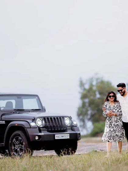 A duplicate of the first image, showing a stylish couple walking hand-in-hand next to a black Mahindra Thar in a rustic, open landscape.