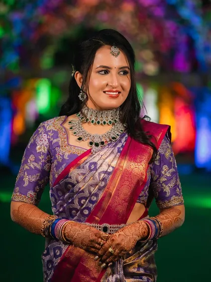 A bride in a rich purple Kanchipuram saree with a matching embroidered blouse. The intricate design work on the blouse complements the saree's traditional patterns.