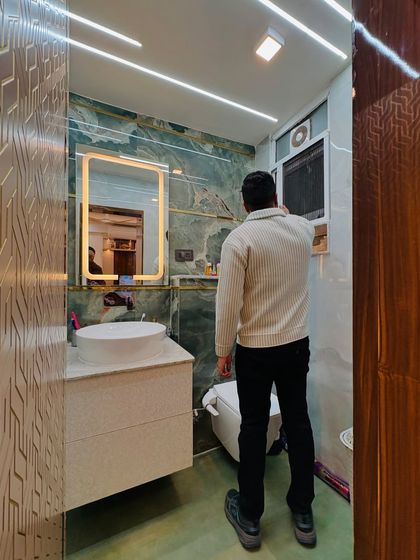 Final inspection of a bathroom renovation. This space features beautiful green onyx-style tiles, a modern vanity, and linear lighting on the ceiling for a bright, luxurious feel.