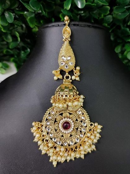 A similar oversized maang tikka with a jhumka drop, this one featuring a red stone.