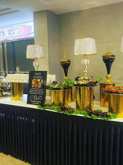 A main course buffet setup for a housewarming luncheon in Rajouri Garden. The black and gold theme with tall decorative vases and lamps creates a sophisticated dining experience within a home setting.