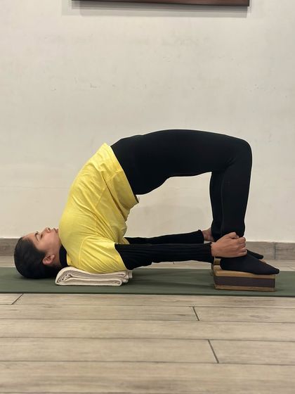 Here is the classic Chatushpadasana, or bridge pose, with hands holding the ankles and a folded blanket supporting the shoulders. This version strengthens the back, glutes, and hamstrings while opening the chest.