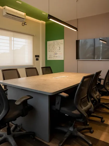 The main conference room is designed for collaboration, with a large central table and ergonomic seating. A whiteboard and wall-mounted screen are integrated for presentations, while a bold green accent wall keeps the space feeling fresh and on-brand.