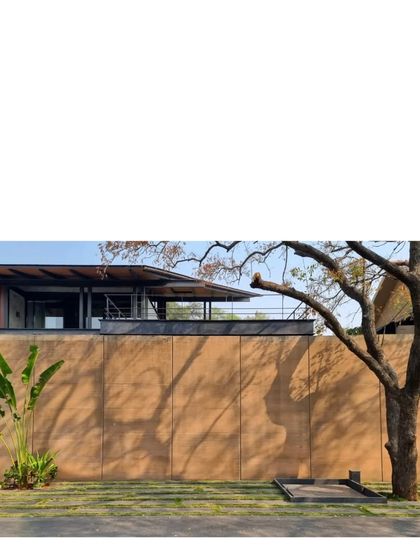 The warm tones of the rammed earth wall contrast with the cool shadows of the trees. This material, taken from the site, keeps the home cool and gives it a sense of place.