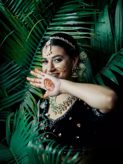 A playful and beautiful shot of the bride. Her traditional makeup, complete with a nath and maang tikka, looks stunning against the lush green background.