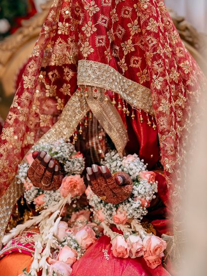 A close-up of the bride's hands holding garlands, with her intricate red and gold wedding attire visible. This is a perfect example of a detail-oriented shot.