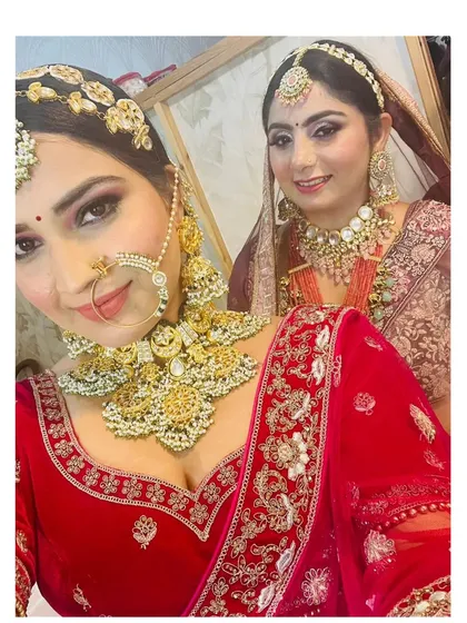 A selfie of two clients in full bridal attire, showcasing the heavy gold jewellery and flawless makeup I provided for their special day.
