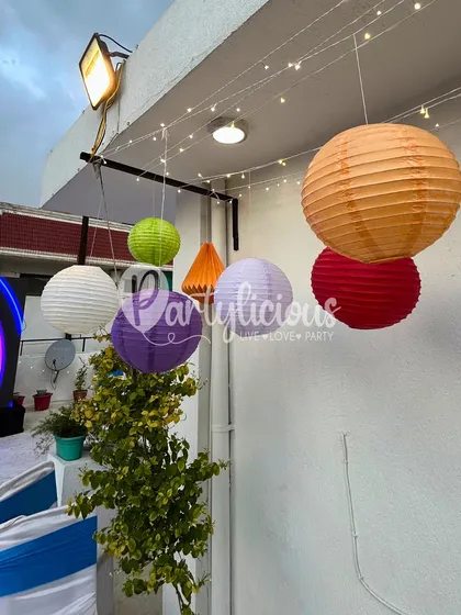 Colorful paper lanterns hanging under fairy lights, adding a festive and whimsical touch to an outdoor party space.