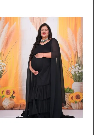 A full-length shot of the mom-to-be in a flowing black dress with sheer cape-like sleeves. The warm, yellow-toned backdrop with pampas grass and sunflowers creates a cheerful and stylish contrast.