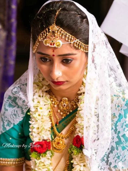 A serene bridal moment during the ceremony. This look features subtle makeup with a bold red lip, complemented by a traditional matha patti and a delicate lace veil.
