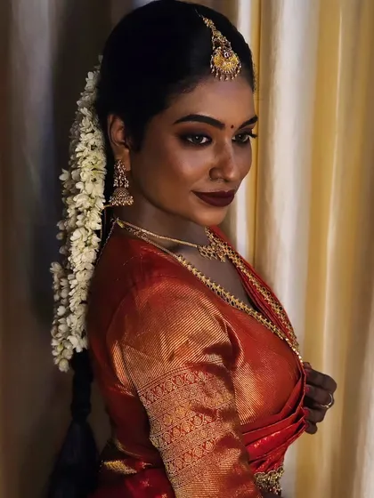 A side profile of a model with deep brown skin, showcasing the beautiful traditional hairstyle and the flawless makeup that enhances her features.
