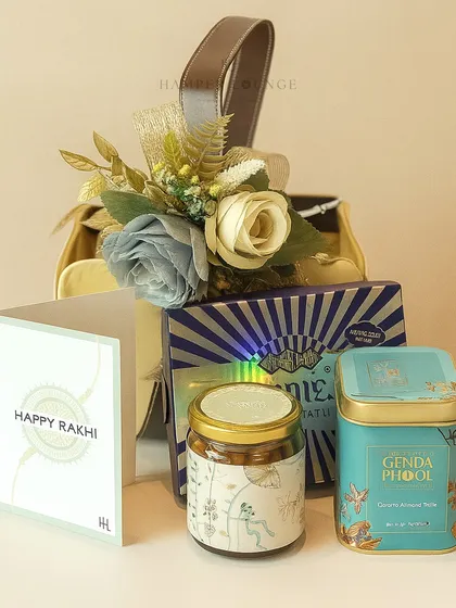 A closer look at the miniature Rakhi hamper. You can see the Genda Phool tea and other gourmet items neatly arranged in the stylish bag, complete with a "Happy Rakhi" card.