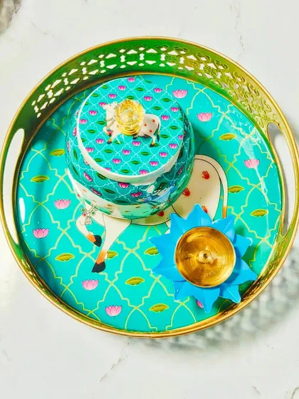 This Pichwai-themed set, featuring a tray, jar, and brass lotus diya, is a stunning centerpiece for your Diwali celebrations. The traditional cow and lotus motif is both beautiful and auspicious.