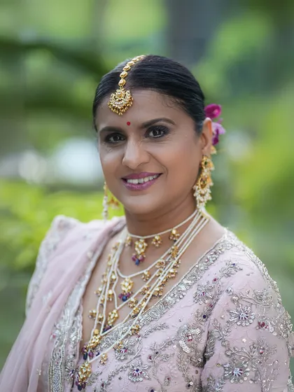 A close-up portrait that captures her happy expression. The makeup features a soft purple smokey eye and a matching lip color, beautifully coordinated with her jewellery.