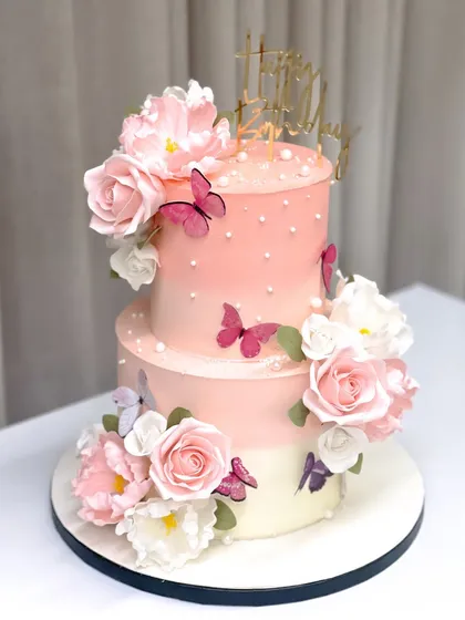 A beautiful 50th birthday cake adorned with handmade sugar flowers and delicate butterflies. The ombre pink ganache provides a soft, feminine backdrop for the intricate details.