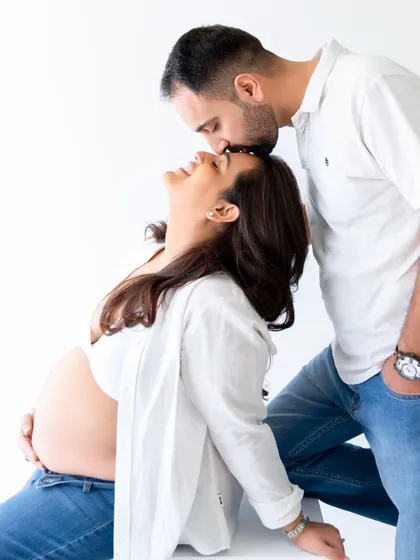 An intimate moment between expecting parents, captured in a bright, minimalist studio setting. This candid couple's pose highlights the connection and joy of pregnancy.