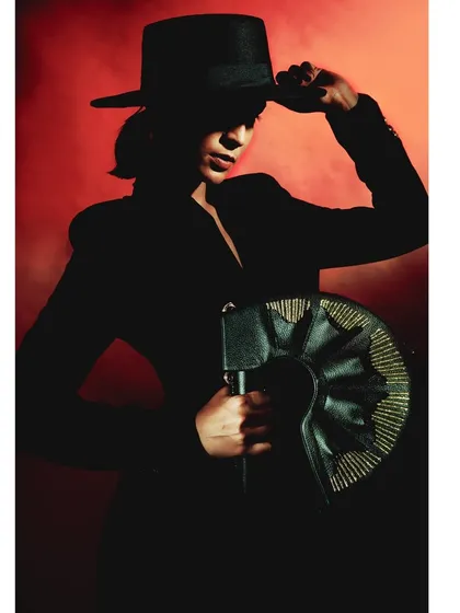 A silhouette shot from 'Levels of Power,' where the model tips her hat. The red background glows behind her, creating a powerful and cinematic image.