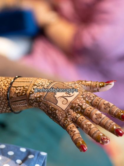 A close-up of a personalized back-hand design. The bride's initial is elegantly placed within a square frame, surrounded by delicate floral patterns.