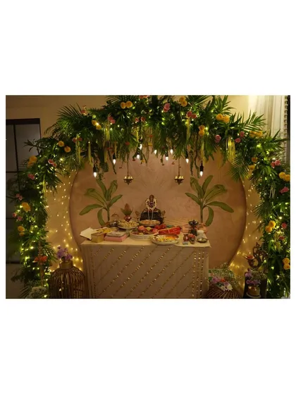 We designed this breathtaking Ganpati mandap, creating a divine focal point for the celebration. The setup features a lush arch of fresh palm leaves and florals, warmly lit by fairy lights and hanging Edison bulbs, all framing a custom-painted backdrop for a truly serene atmosphere.