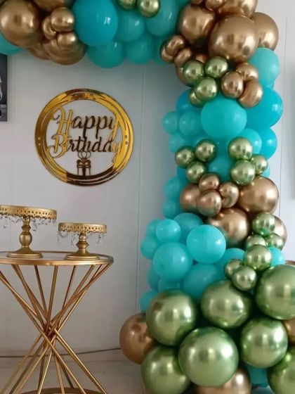 This balloon arch in shades of teal, green, and gold adds a touch of elegance to any home party. Paired with gold cake stands, it creates a beautiful and cohesive dessert table display.