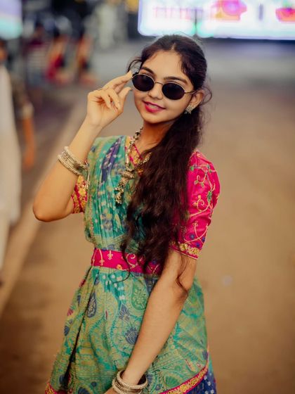 A close-up shot of another attendee in a beautiful green and pink traditional outfit. Her round sunglasses add a quirky and fun element.