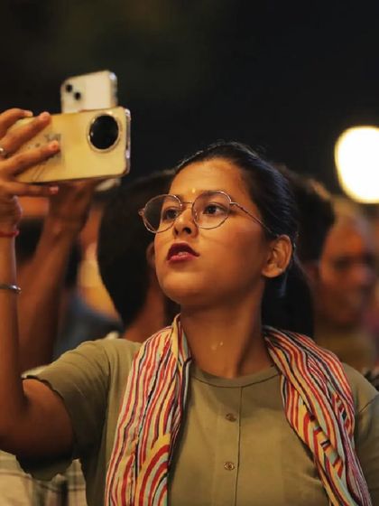 A young woman films the drone show in Varanasi, her face lit by her phone and the lights in the sky. Capturing these moments of wonder is what our work is all about.