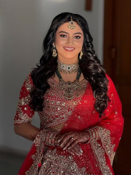 A happy, smiling portrait of the bride in her red reception lehenga. The makeup is bright and enhances her joyful expression.