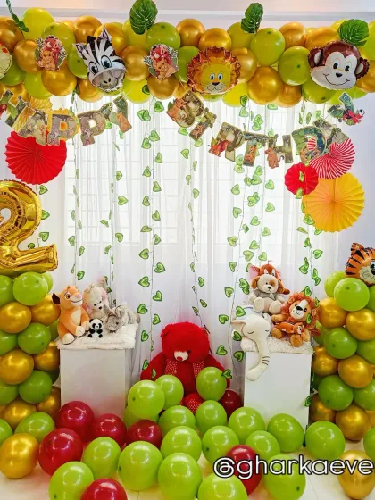 A classic jungle theme setup for a 2nd birthday, using green and gold balloons and plush animal toys as props.