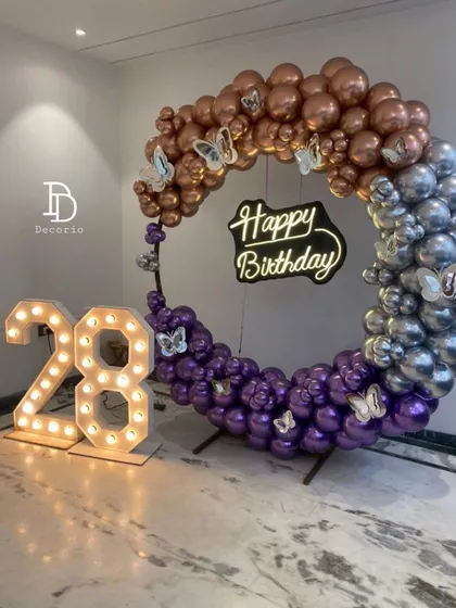A sophisticated 28th birthday ring setup with a beautiful blend of metallic colors. The circular frame is decorated with rose gold, silver, and purple balloons, along with light-up '28' numbers and a neon sign.