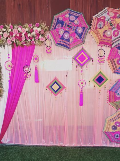 A clear, bright shot of the pink-themed Mehendi backdrop. The combination of the floral L-frame, the Rajasthani umbrellas, and the traditional hangings creates a rich and festive look.