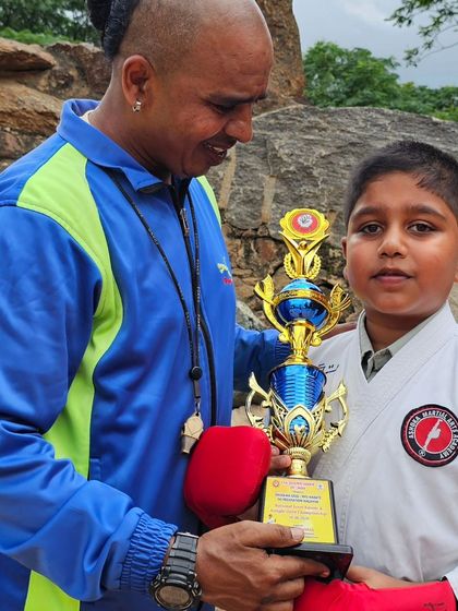 This young student, equipped with his sparring gloves, proudly holds his trophy. He is on the path to becoming a great martial artist.