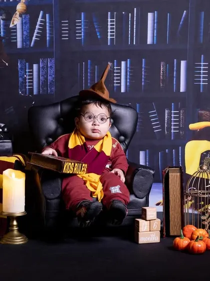 A baby dressed as a wizard, sitting in a large chair with a sorting hat, set against a magical library backdrop.