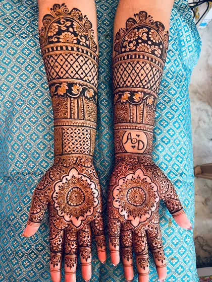 This bridal mehendi combines a central floral mandala on the palm with dense, geometric patterns on the arms. The couple's initials are subtly included, adding a personal touch to the traditional design.