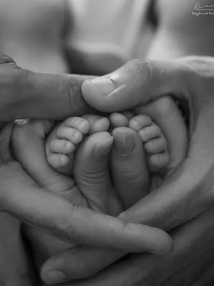 A family's hands gently holding a newborn's tiny feet. This powerful black and white image symbolizes love, protection, and unity.
