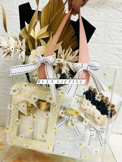 A handheld view of the all-white luxury hamper, showing the beautiful arrangement of gifts inside the daisy-printed PVC bag.