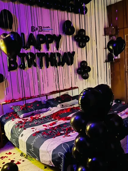 For a more modern and bold look, I offer themes like this all-black birthday decoration. The setup includes black foil letters, black heart-shaped balloons, and a shimmery silver curtain backdrop, with red rose petals on the bed for a touch of color.