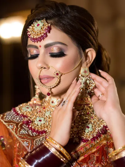 A close-up of a bride adjusting her earring, showing off the glittery eye makeup and flawless base.