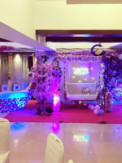 A wide view of an elaborate baby shower stage with a large floral moon, a decorated swing, and multiple baby-themed cutouts, perfect for a grand celebration.
