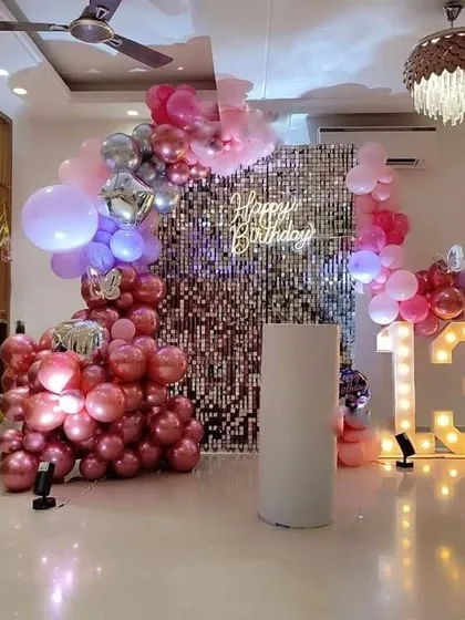 A 13th birthday party with a silver sequin wall. The decoration features a pink and purple balloon arrangement, a "Happy Birthday" neon sign, and marquee numbers.