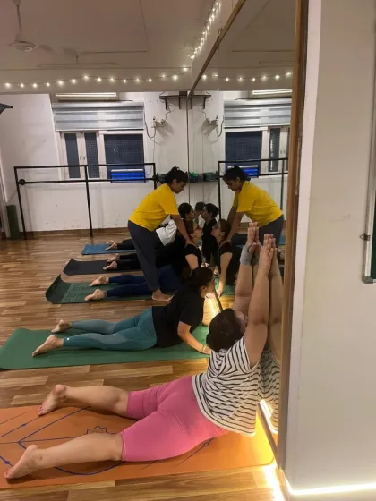 An instructor assists a student in Bhujangasana (Cobra Pose) using the wall, a technique that helps deepen the backbend while protecting the lower back.