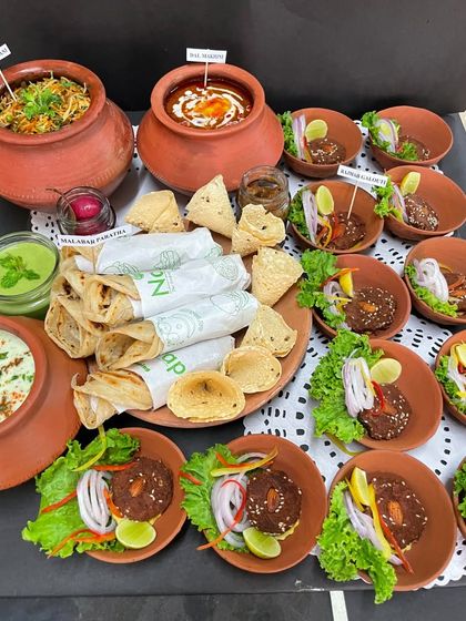 An elaborate Indian meal platter featuring Galouti Kebabs, Malabar Parathas, Biryani, and Dal Makhani, all served in traditional terracotta pottery.