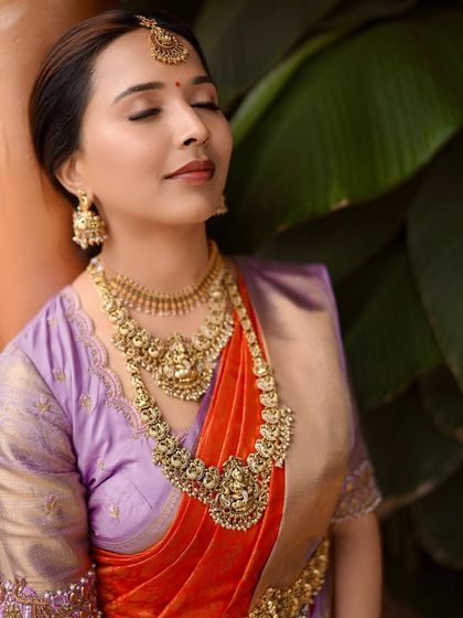A close-up of our client Anusha, serene and beautiful on her engagement day. The rich temple jewelry perfectly complements the intricate zari work on her lavender and red silk saree.